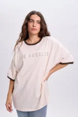 Remera oversize de manga corta en color crudo, con cuello redondo y puños en tono marrón oscuro. Cuenta con el texto "Los Angeles" estampado en el frente.