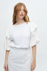Blusa blanca con bordado calado, mangas abullonadas y volados en los hombros.
