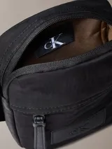 Cartera bandolera Calvin Klein color negro, confeccionada en nylon reciclado. Presenta correa ajustable, cierre superior con cremallera, bolsillo frontal y logo CK en relieve.
