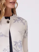 Cárdigan de punto marca Sioni, color beige con estampado floral en tonos azules. Presenta escote redondo a la base, cierre frontal con un botón metálico y mangas largas de corte recto.