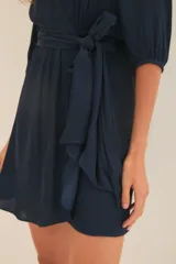 Vestido corto azul marino de manga larga con efecto abullonado en puños, escote cruzado en V y lazo ajustable en la cintura.