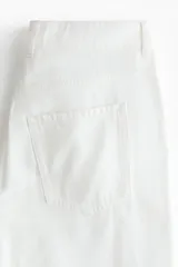 Jean de cinco bolsillos en denim rígido, de color blanco, con piernas amplias, corte holgado y cintura estándar con cierre y botón.