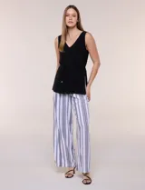 Enterito de efecto dos piezas con parte superior negra lisa, escote en V y sin mangas, y parte inferior de pantalón palazzo de corte amplio con diseño a rayas en blanco y negro. Cuenta con cintura entallada con lazo ajustable.