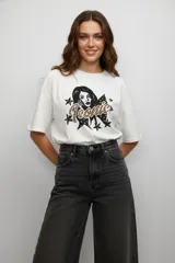Remera de algodón color gris topo, de corte holgado y diseño cropped. Presenta cuello redondo y una estampa frontal con forma de corazón, mariposa y texto decorativo.