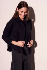 Sobrecamisa negra de estilo shacket, confeccionada en tejido de gamuza sintética. Presenta cuello camisero, cierre frontal de botones y dos bolsillos de parche con solapa en el pecho. El calce es oversize y las mangas son largas.