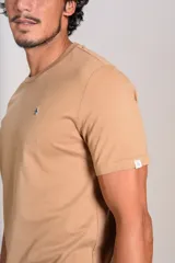 Remera de manga corta con cuello redondo, confeccionada en algodón de color beige. Presenta un pequeño logo bordado de un pingüino en el pecho.