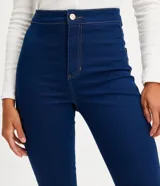 Pantalón de jean azul oscuro, corte skinny, tiro alto, con trabillas en la cintura, cierre con botón y cremallera, y dos bolsillos traseros.