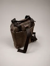 Matera mochila unisex de cuero marrón, con diseño estructurado, bolsillo frontal con cierre, asas superiores y correas ajustables.