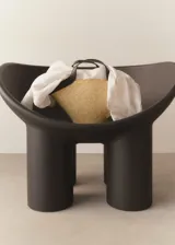 Bolso tipo capazo de fibras naturales con estructura rígida en forma de abanico, con detalles en cuero sintético negro en los bordes superiores y asas. Incluye una correa larga ajustable y cierre de nudo.
