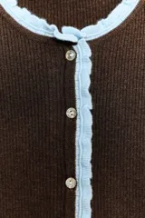 Chaqueta de punto marrón de manga corta, con cuello redondo y ribetes en color celeste claro. Presenta cierre frontal con botones nacarados.