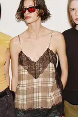 Top lencero de escote en pico con tirantes finos ajustables. Presenta un estampado de cuadros en tonos beige y marrón, con detalles de encaje negro en el escote y en el ruedo.