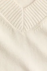 Buzo oversized de punto suave, color beige, con escote en V acanalado, hombros caídos y mangas largas. Cuenta con ribetes acanalados en los puños y en el dobladillo inferior.