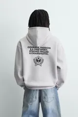 Sudadera con capucha y bolsillo frontal tipo canguro, confeccionada en tejido de algodón con interior perchado. Presenta diseño de corte boxy fit, mangas largas con puños y ruedo en rib, y texto bordado y estampado en el frente.