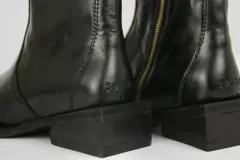 Bota de cuero color negro con punta cuadrada, suela de cuero y taco cuadrado. Presenta cierre lateral de metal plateado y herraje metálico decorativo en el lateral.