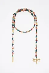Collar largo estilo lariat o bolo, compuesto por piedras semipreciosas facetadas y pulidas de múltiples colores, intercaladas con pequeñas cuentas negras. Termina en dos extremos colgantes: uno con un tubo metálico dorado y el otro con una perla blanca, seguido de más piedras y un dije grande con forma de libélula dorada.