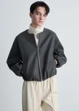 Chaqueta tipo bomber de color gris oscuro, con cuello redondo, cierre frontal de cremallera y diseño oversize. Presenta mangas largas con puños elásticos fruncidos y detalle fruncido en el bajo, además de dos bolsillos laterales.
