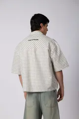 Camisa de manga corta de popelina con patrón a cuadros, calce boxy y largo a la cintura, con bolsillos y canesú cortados en diagonal.