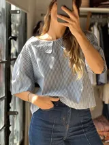Blusa celeste y blanca a rayas verticales, con corte boxy, mangas cortas amplias y cuello Peter Pan.