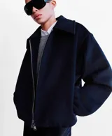 Chaqueta de corte amplio y estructurado en color negro, con cuello solapa, cierre frontal de cremallera metálica y bolsillos laterales discretos.