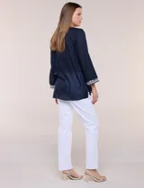 Blusa de corte holgado de inspiración étnica con bordados ornamentales blancos a contraste. Presenta escote en V pronunciado con pechera bordada con motivos arabescos y florales, mangas largas y aberturas laterales en el ruedo.