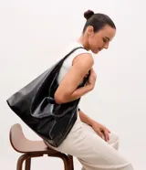 Cartera estilo hobo de gran tamaño, color negro, con superficie texturizada de líneas verticales. Presenta un diseño de media luna con asa ancha fija y abertura superior amplia.