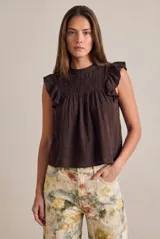 Blusa marrón de corte oversize y sin mangas, con cuello redondo y detalles fruncidos en el pecho. Presenta volados decorativos en los hombros y diseño fluido.