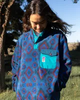 Buzo de polar fleece con diseño estampado geométrico en tonos azules, bordó y verde. Presenta cuello alto con cierre de botones a presión, bolsillo frontal con solapa en contraste color turquesa y puños elásticos.