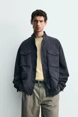 Cazadora regular fit de algodón color gris oscuro con efecto lavado, cuello subido, manga larga y cierre frontal con cremallera oculta por solapa con botones a presión. Cuenta con cuatro bolsillos frontales de plastrón con solapa y cintura ajustable con cordón interior.