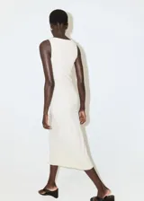 Vestido midi color beige de silueta slim, sin mangas y con cuello barca. Presenta frunces sutiles en los laterales de la cintura.