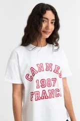 Remera de manga corta color beige, con estampa frontal en tono azul con la leyenda "New York 1990", de corte holgado y diseño casual.
