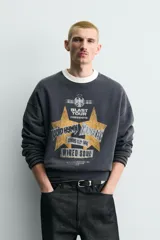 Sudadera de corte boxy fit en color gris oscuro con efecto lavado. Presenta cuello redondo en contraste color crema, manga larga con puños acanalados y estampado gráfico frontal con estrellas y tipografía estilo vintage.