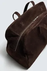 Bolso de viaje de gran tamaño confeccionado en piel con acabado de serraje. Cuenta con un compartimento principal con cierre de cremallera e imanes, interior con bolsillo con cierre y bolsillo plano, y dos asas de mano de piel.