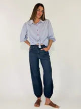 Pantalon de denim azul oscuro con diseño abombado y puños fruncidos con elástico en los tobillos. Cuenta con bolsillos laterales y cierre frontal con botón y cremallera.