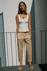 Pantalón chino beige de tiro bajo, con pernera recta y bajo con vuelta. Incluye bolsillos delanteros, falsos bolsillos traseros con solapa y cierre frontal con cremallera y botón. Viene acompañado de un cinturón trenzado marrón.