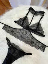 Conjunto de lencería de tres piezas en encaje negro. Incluye bralette con breteles regulables, collarín integrado con cuello ajustable y tanga regulable con corte media less.