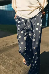 Pantalón de tiro medio con cintura elástica y bolsillos ocultos en costura. Presenta un diseño de corte recto con dobladillo ancho en el bajo y un estampado geométrico sobre fondo oscuro.