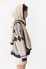 Bufanda de punto color marrón con capucha integrada y bordes en color crema. Presenta una etiqueta rectangular bordada con la palabra Anthea en uno de sus extremos.