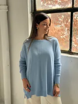 Sweater de punto color celeste, con cuello redondo, corte holgado y mangas largas con puños acanalados. Presenta un detalle de costura vertical central en el frente.
