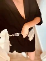 Cinturón de cuero negro con hebilla plateada y riñonera plateada con flecos.