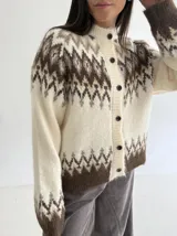 Cardigan de punto con diseño jacquard de inspiración nórdica, en tonos blanco, gris y marrón. Presenta cuello redondo, cierre frontal con botones y mangas largas con puños acanalados.