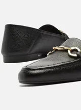 Mocasín de cuero negro con detalle de hebilla dorada.