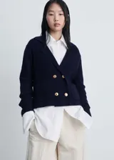 Chaqueta de punto azul marino con diseño cruzado y doble botonadura con botones dorados efecto joya. Presenta cuello con solapas, manga larga y dos bolsillos de parche frontales.