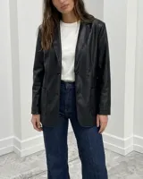 Blazer de corte recto confeccionado en cuerina negra, con solapas clásicas, cierre frontal de dos botones y bolsillos laterales aplicados.
