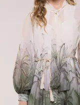 Vestido corto de gasa estampada con motivos botánicos en tonos verdes y crudo, diseñado por Julia Jordan. Cuenta con cuello alto con lazo para atar, abertura frontal con botones, delantera plisada, mangas largas abullonadas y un lazo ajustable en la cintura. Incluye forro interno.