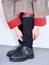 Bota híbrida de caña alta confeccionada en lona negra en la parte superior y cuero negro en la base tipo mocasín, con plataforma, suela track y tira con hebilla metálica cruzada en el empeine.