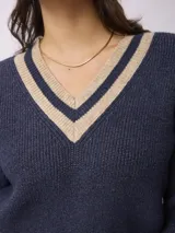 Sweater de punto estilo preppy, color blanco con detalles de rayas negras en el escote en V, puños y ruedo. De corte holgado y manga larga.