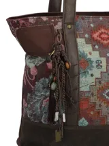 Cartera tipo tote con diseño patchwork que combina paneles de tela estampada con motivos geométricos y florales en tonos tierra, burdeos y azul, con detalles en cuero sintético marrón. Cuenta con manijas fijas, cierre principal con cremallera y un llavero decorativo con borlas y cuentas colgando de uno de los laterales.