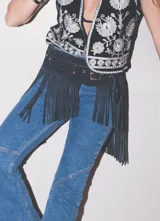 Cinto negro de cuero con diseño ancho adornado con largos flecos colgantes y hebilla metálica.
