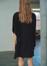 Vestido corto negro de corte recto con cuello alto y mangas asimétricas. Cuenta con cierre posterior de cremallera y botones.
