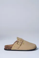 Zueco beige con diseño cerrado al frente, tira con hebilla dorada y detalles de tachas metálicas. Suela de corcho y base de goma estriada.